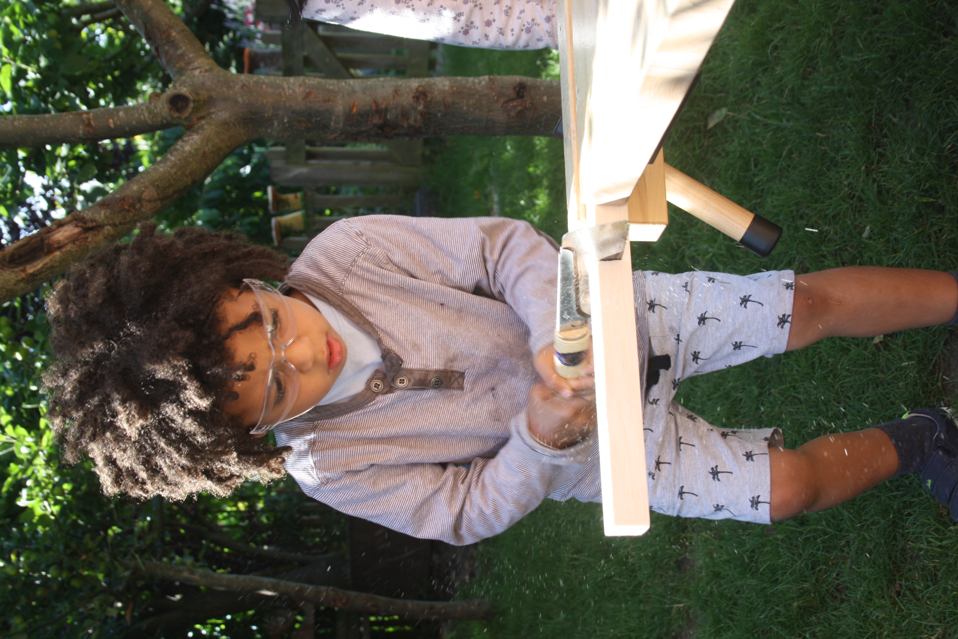 A child uses a small saw to cut wood.