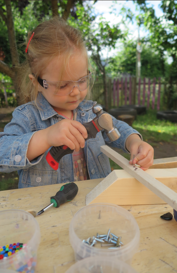 A child uses a hammer to nail two pieces of wood together.