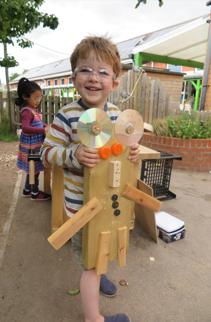 A child shows the robot they created during a woodworking project.