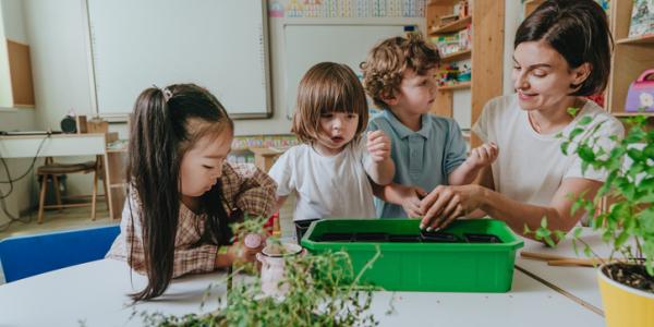 a teacher and students observing plants in a tray of soil