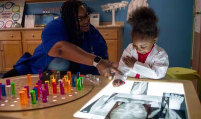 A teacher works with a child at the light table.