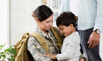 a military mom in camo gear giving her young child a hug