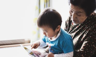 Preschool boy in his grandma's lap, learning on a tablet