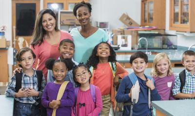 Two teachers and a group of young children standing and smiling in the classroom.