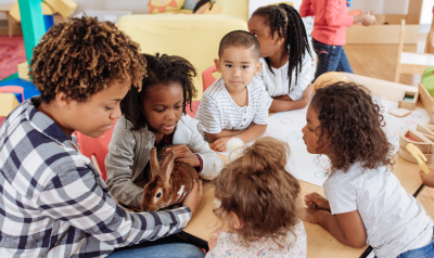 a teacher and children petting a bunny in a classroom