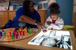 A teacher works with a child at the light table.