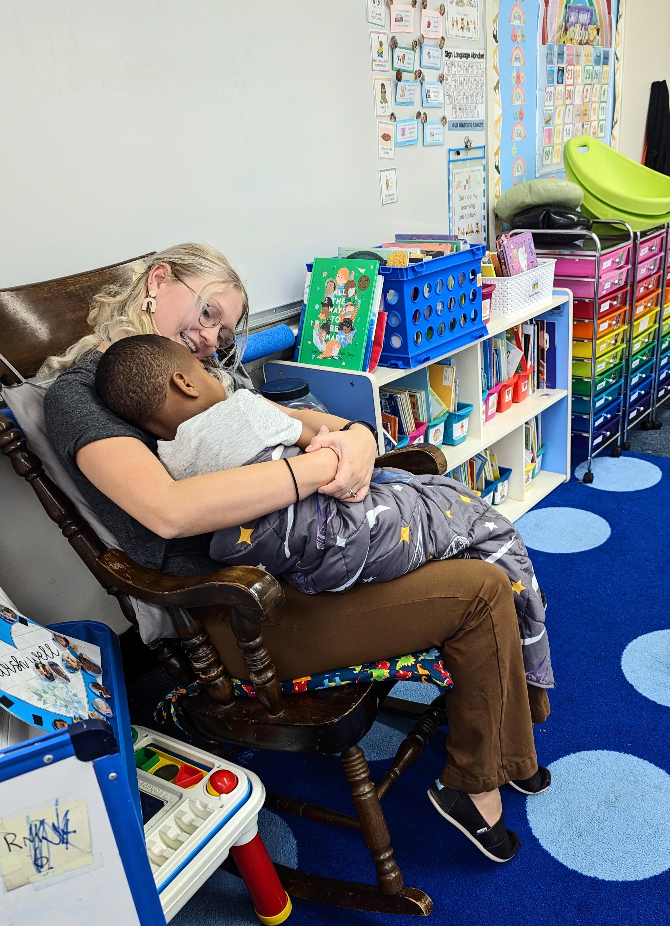 A teacher rocks a child and talks to him.